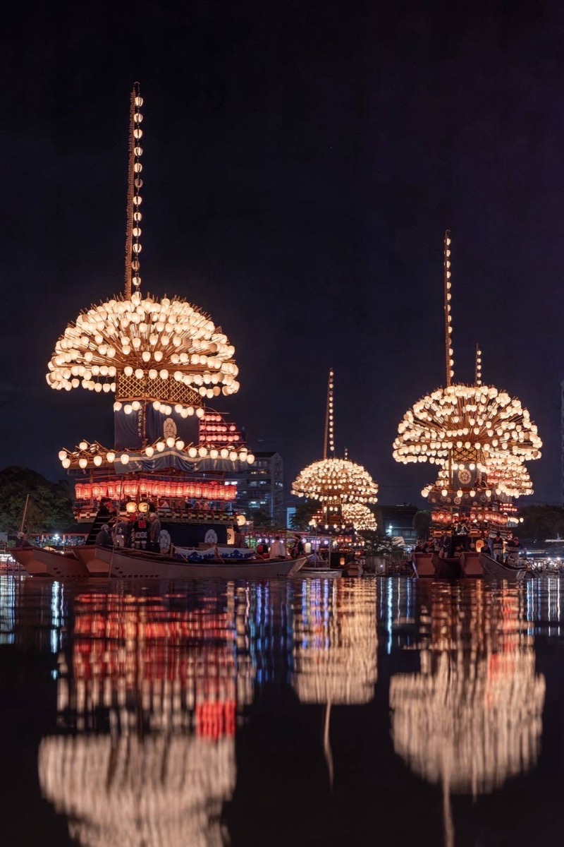 Lantern-covered festival boats lit up at night and reflected in the water